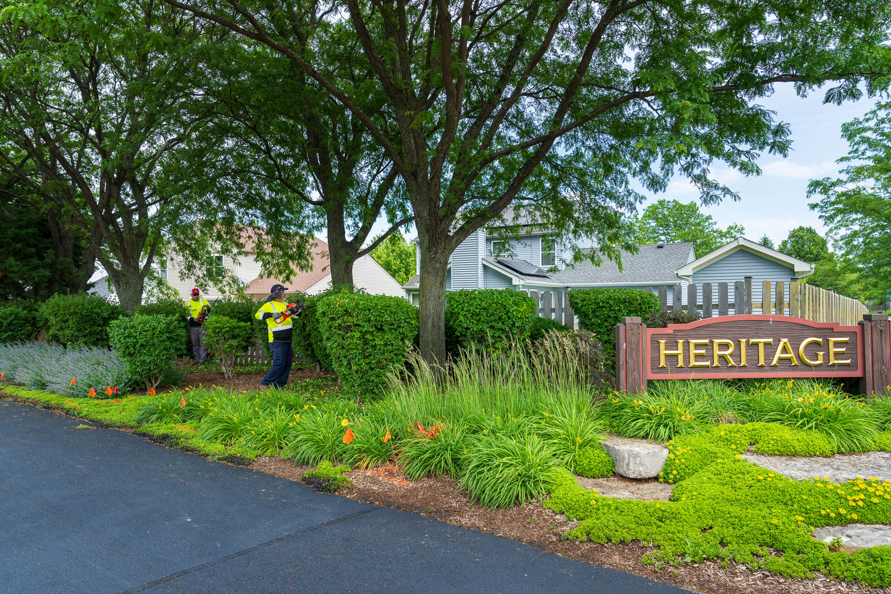 landscape crew pruning trimming up hedges bushes near HOA landscape entrance sign